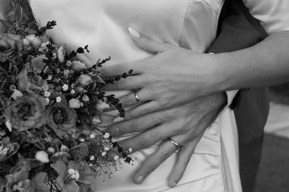 A black and white close-up of an affectionate wedding couple embracing with bridal bouquet.